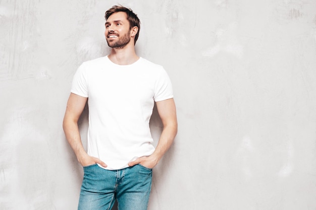 Portrait of handsome smiling stylish hipster lambersexual model sexy man dressed in tshirt and jeans fashion male isolated on blue wall in studio