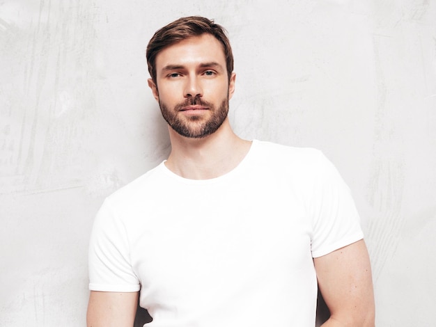 Portrait of handsome smiling stylish hipster lambersexual model Sexy man dressed in Tshirt and jeans Fashion male isolated on blue wall in studio