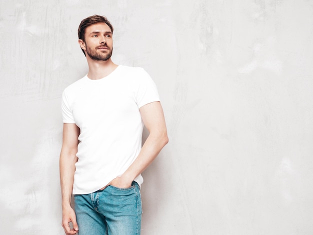 Portrait of handsome smiling stylish hipster lambersexual model Sexy man dressed in Tshirt and jeans Fashion male isolated on blue wall in studio