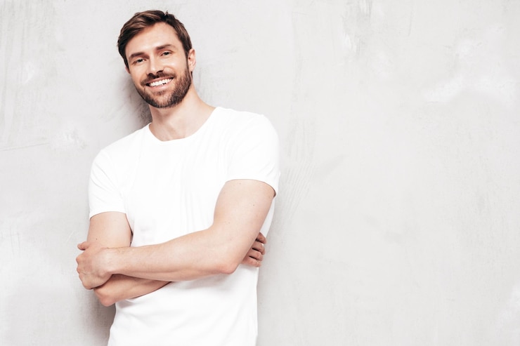 Free Photo portrait of handsome smiling stylish hipster lambersexual model sexy man dressed in tshirt and jeans fashion male isolated on blue wall in studio
