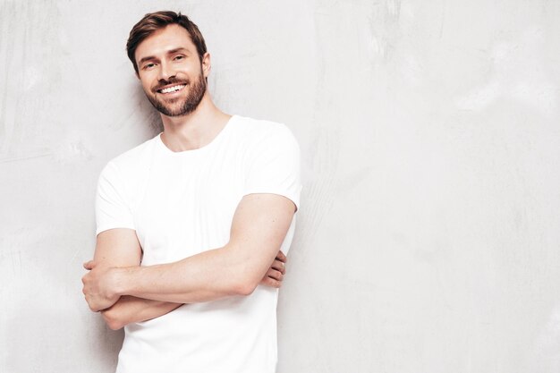 Portrait of handsome smiling stylish hipster lambersexual model Sexy man dressed in Tshirt and jeans Fashion male isolated on blue wall in studio