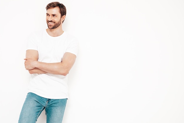 Портрет красивого улыбающегося стильного хипстера-ламберсексуала модели Сексуальный мужчина, одетый в футболку и джинсы Модный мужчина, изолированный на белой стене в студии