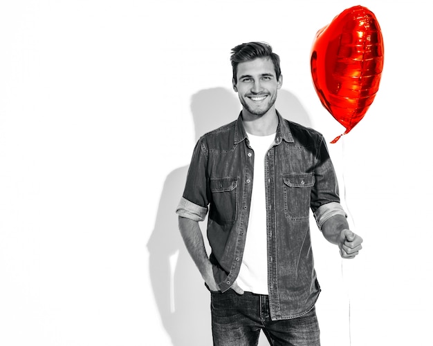 Portrait of handsome smiling stylish man model dressed in jeans clothes. Fashion man holding heart shaped balloon. 