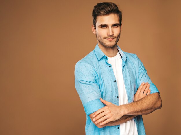 Portrait of handsome smiling stylish young man model dressed in blue shirt clothes. Fashion man posing. Crossed arms