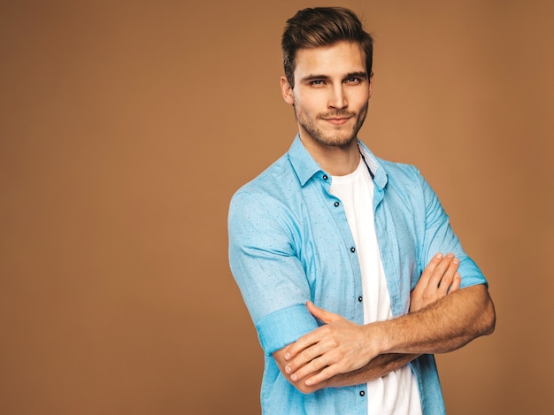 Portrait of handsome smiling stylish young man model dressed in blue shirt clothes. Fashion man posing. Crossed arms