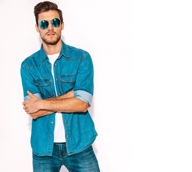 Portrait of handsome smiling stylish young man model wearing jeans clothes and sunglasses. Fashion man .Crossed arms