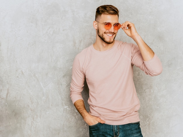 カジュアルな夏のピンクの服を着てハンサムな笑みを浮かべて若い男モデルの肖像画。丸いサングラスでポーズをとってファッションスタイリッシュな男