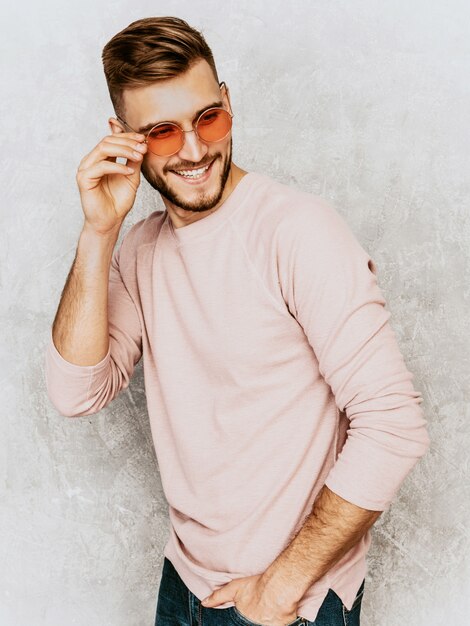 Portrait of handsome smiling young man model wearing casual summer pink clothes. Fashion stylish man posing in round sunglasses