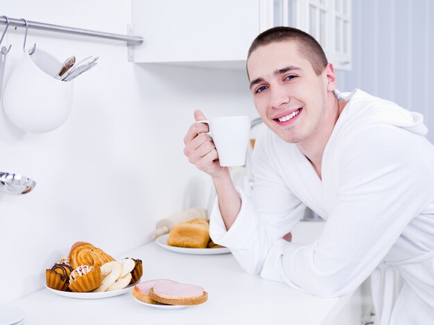 キッチンでカップとハンサムな笑顔の若い男の肖像画