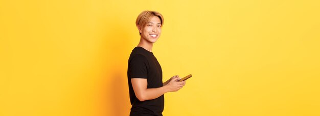 Free photo portrait of handsome stylish asian guy in black outfit using mobile phone and turning head at camera
