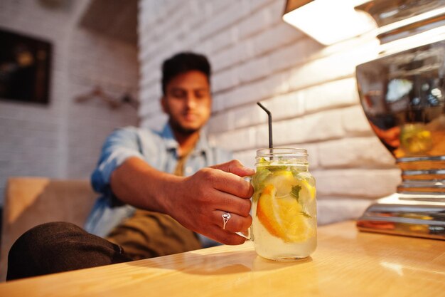 Portrait of handsome successful bearded south asian young indian freelancer in blue jeans shirt sitting in cafe with lemonade