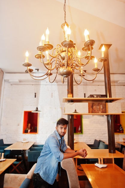 Portrait of handsome successful bearded south asian young indian freelancer in blue jeans shirt standing in cafe