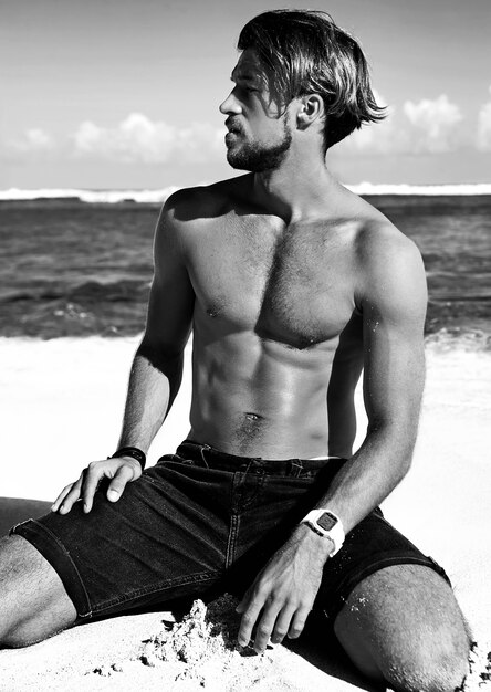 Portrait of handsome sunbathed fashion man model posing on summer beach 