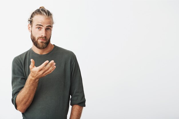 Portrait of handsome swedish man with trendy hairdo and beard in casual grey clothes looking