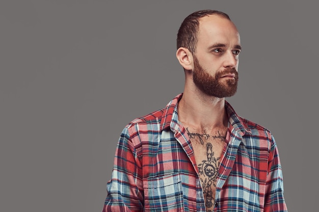 Portrait of a handsome tattooed stylish hipster with a well-trimmed beard in a flannel shirt, posing in a studio. Isolated on a gray.