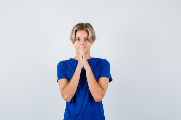 Portrait of handsome teen boy keeping hands in praying gesture in blue t-shirt and looking hopeful front view