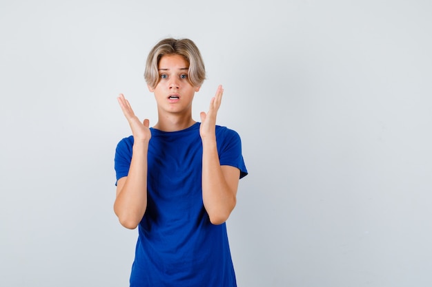 Portrait of handsome teen boy showing surrender gesture in blue t-shirt and looking terrified front view