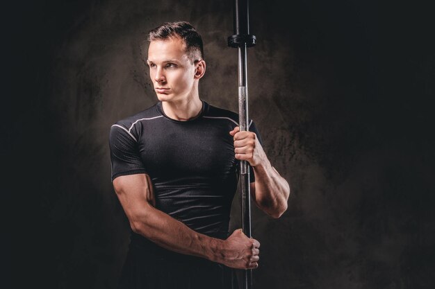 Portrait of a handsome young bodybuilder holding a barbell and looking away on a dark background.