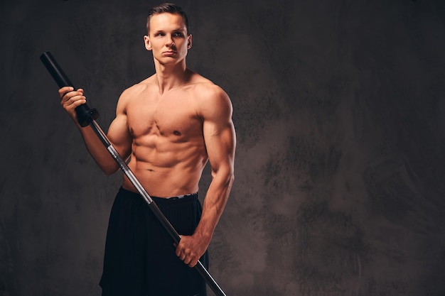 Portrait of a handsome young bodybuilder holding a barbell and looking away on a dark background.