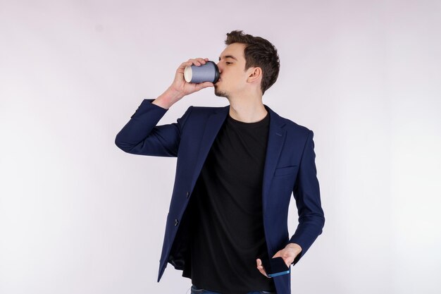 Portrait of a handsome young businessman standing and drinking coffee isolated white background