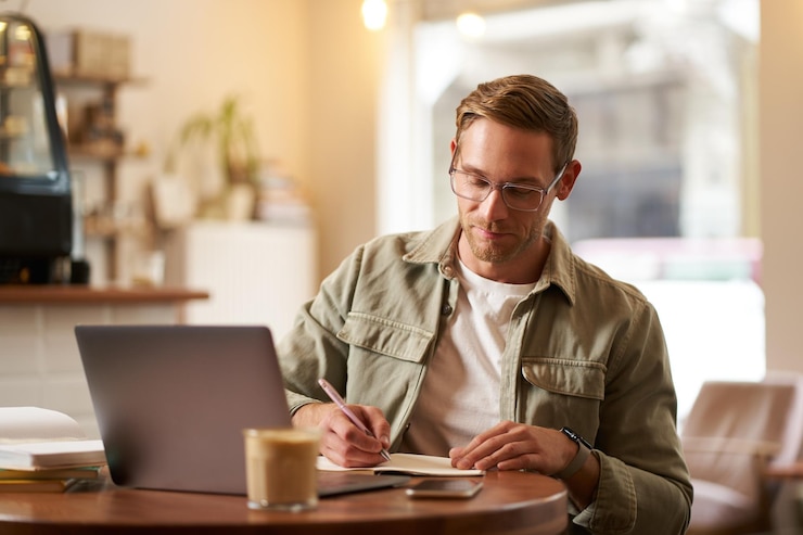 Free Photo portrait of handsome young guy in glasses man studying taking notes looking at laptop screen during