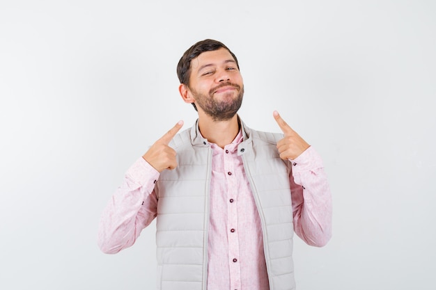 Portrait of handsome young male pointing at his smile in shirt, vest and looking cheerful front view