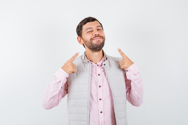 Portrait of handsome young male pointing at his smile in shirt, vest and looking cheerful front view