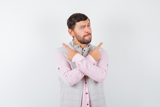 Portrait of handsome young male pointing left and right in shirt, vest and looking indecisive front view
