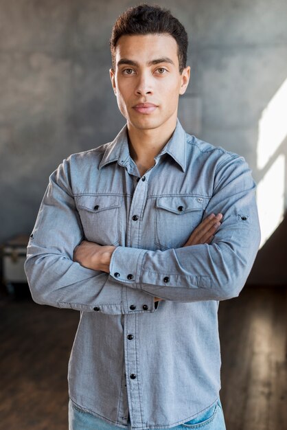 Portrait of a handsome young man in denim shirt with his arm crossed looking at camera