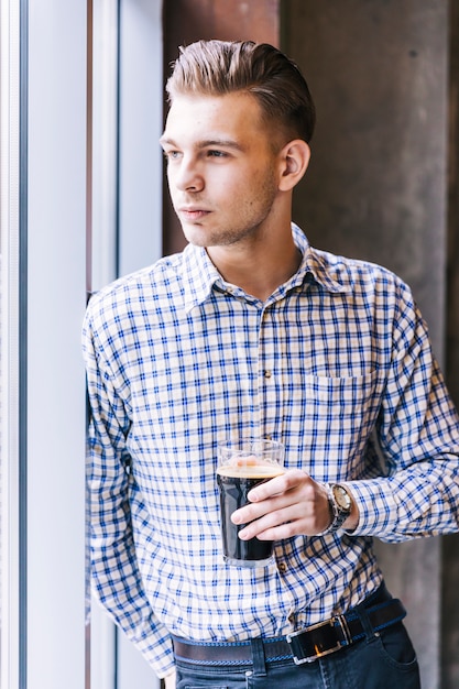 Free photo portrait of a handsome young man leaning at window holding the beer glass