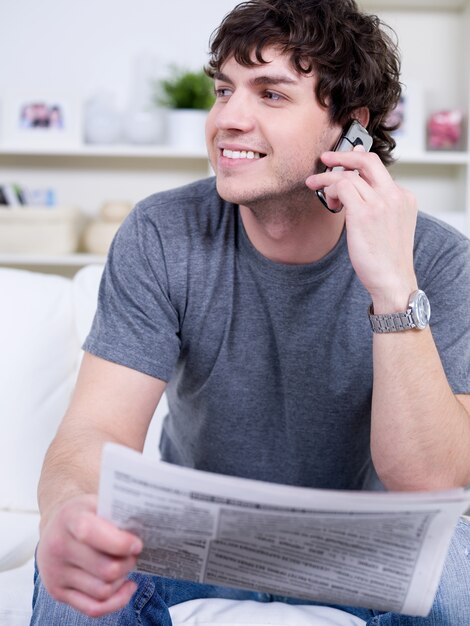 Ritratto di bel giovane che parla al telefono e che tiene il giornale