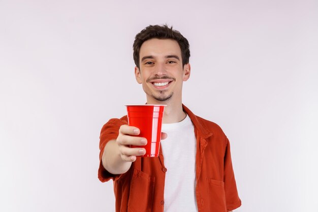 Портрет красивого молодого человека, стоящего и показывающего кофе, глядя на камеру на белом фоне