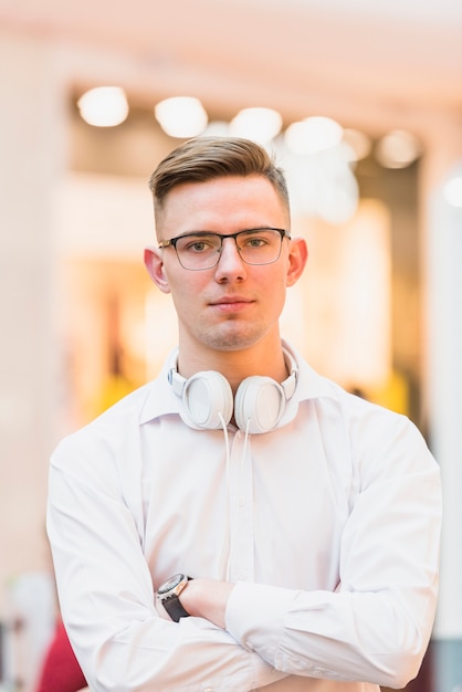 portrait of handsome young man with arms crossed holding white headphone around his neck