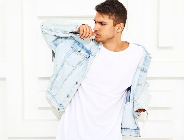 Portrait of handsome young model man dressed in jeans clothes posing near white textured wall