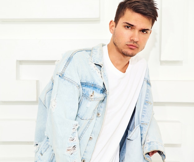Free photo portrait of handsome young model man dressed in jeans clothes posing near white textured wall