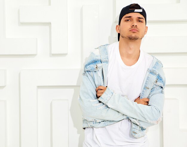 Portrait of handsome young model man dressed in jeans clothes posing near white textured wall