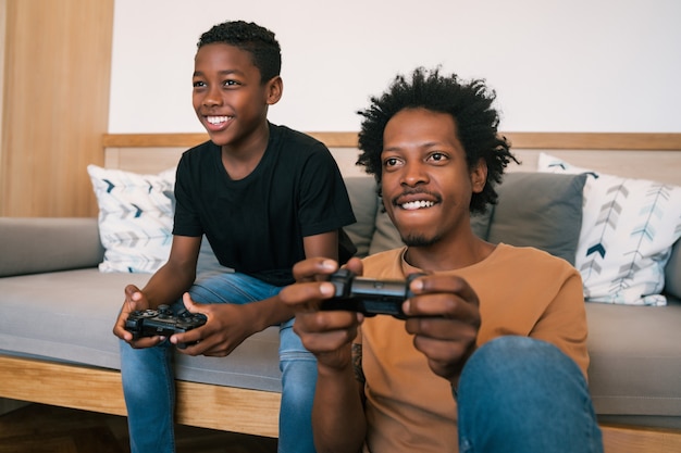 소파 소파에 앉아 집에서 함께 콘솔 비디오 게임을 하는 행복한 아프리카계 미국인 아버지와 아들의 초상화