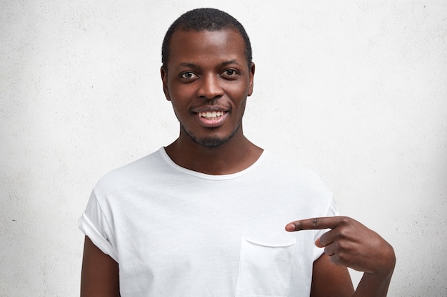 Portrait of happy African American male with pleased expression, smiles gladfully, advertizes new outfit, satisfied after going shopping