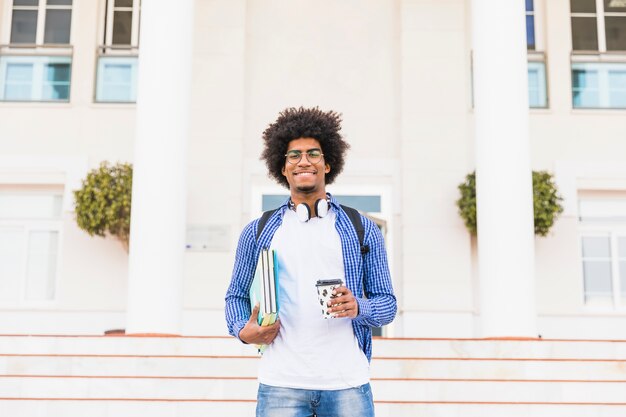 대학 앞에 서서 테이크 아웃 커피 컵을 들고 행복 아프리카 십대 남성 학생의 초상화