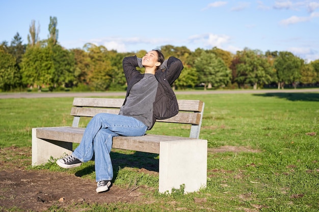 Portrait of happy asian girl feeling freedom and excitement stretching hands while sitting on bench