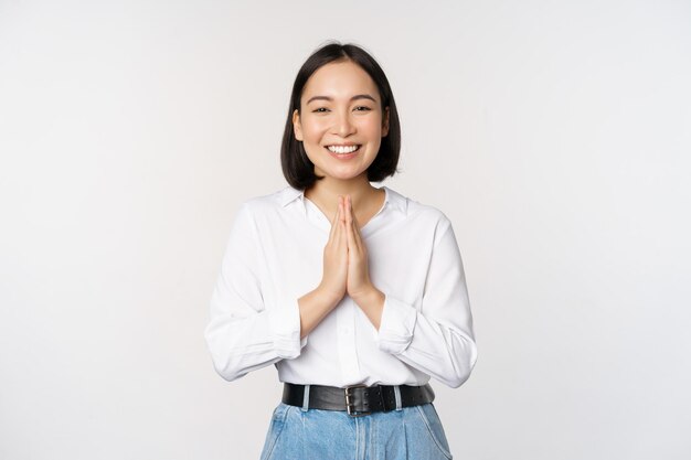 Portrait of happy asian girl laughing and smiling showing thank you namaste gesture grateful for smth standing over white background