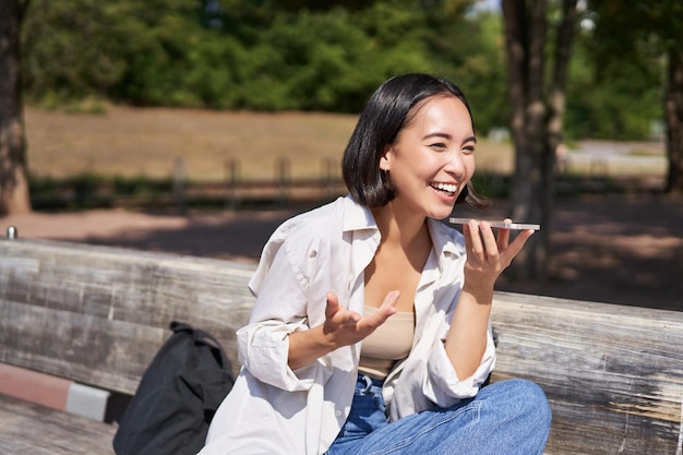 自由快乐的亚洲女孩的画像照片记录语音信息说通过扬声器在智能手机坐在再保险