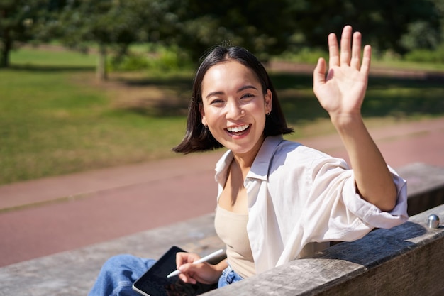 幸せなアジアの女の子の肖像画は、グラフィック ペンと手を振ってデジタル タブレットでの描画を停止すると言う