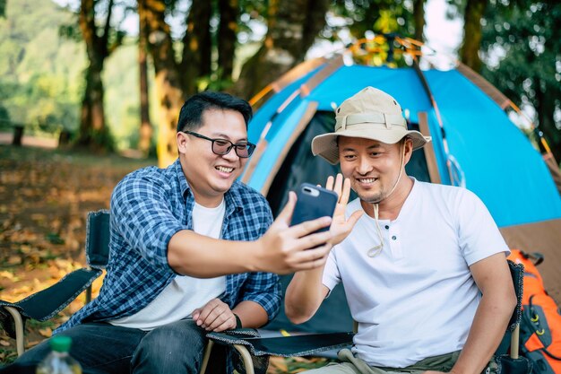 Портрет счастливых азиатских друзей-мужчин, делающих видеозвонок со смартфоном в кемпинге.