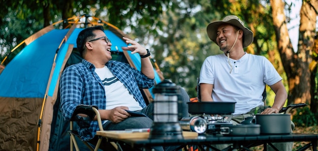 肖像画幸せなアジア人の友人がキャンプで椅子に座って話している料理セットの最前線アウトドアクッキング旅行キャンプライフスタイルのコンセプト