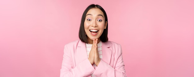 Портрет счастливой азиатской офисной леди, генерального директора, деловой женщины в костюме, радующейся и смеющейся победе, празднующей достижение цели и радующейся стоя на розовом фоне