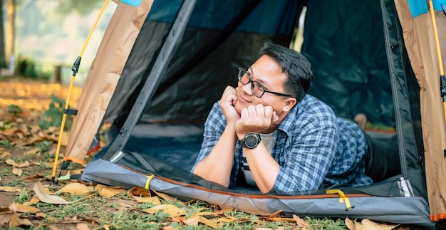 Portrait of Happy Asian traveler man glasses lying in tent camping Outdoor traveling camping and lifestyle concept