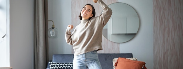 Free photo portrait of happy asian woman dancing rejoicing and triumphing feeling upbeat at home