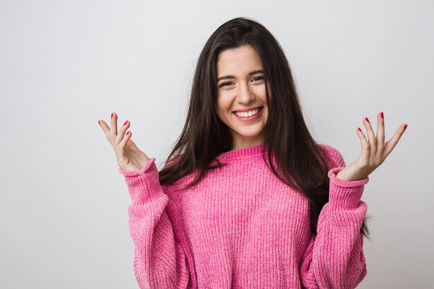 Portrait of happy attractive woman in warm pink sweater, long hair, natural look, sincere smile, positive mood, holding hands up, feeling surprised, isolated