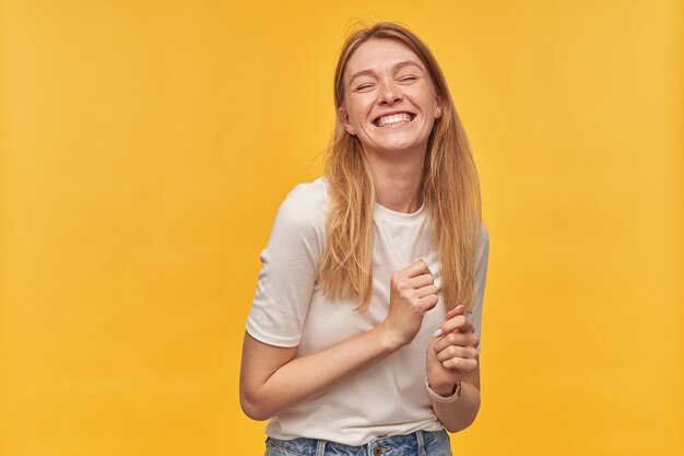 Portrait of happy attractive woman with freckles in white tshirt laughing dancing feels relaxed and having fun on yellow